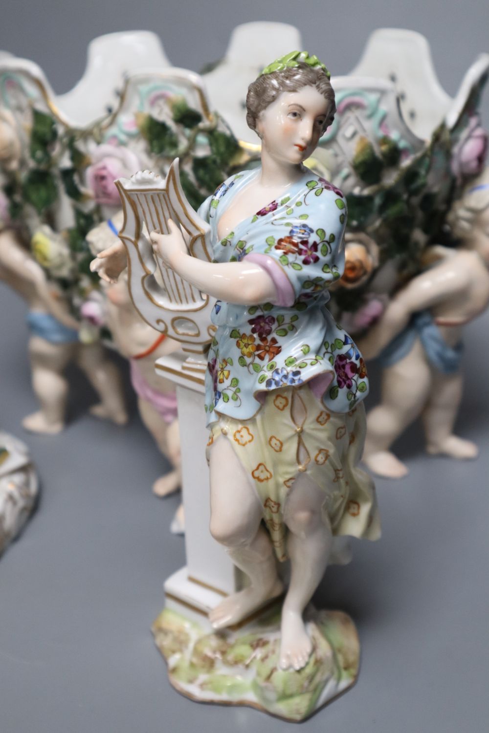 A Meissen style flower-encrusted reticulated oval porcelain jardiniere with cherub supports and three other items,